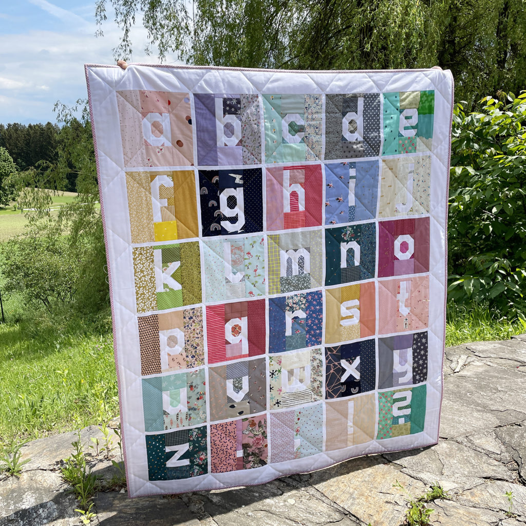 Scrappy Letter Quilt hochgehalten im Garten