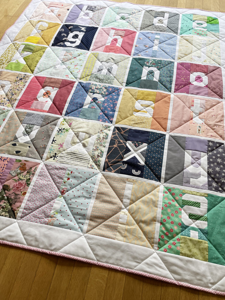 Auschnitt Scrappy Letter Quilt mit diagonalen Linien gequiltet und rosa Binding