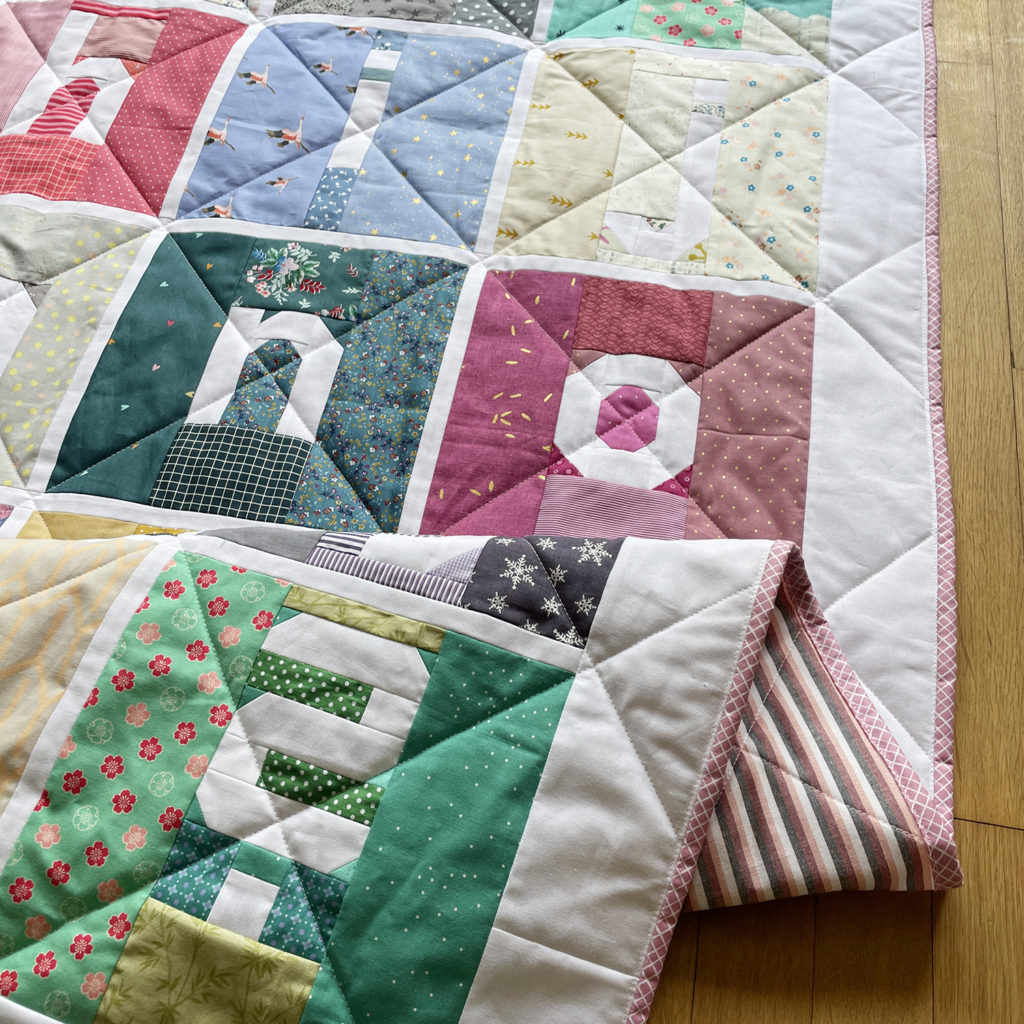 Auschnitt Scrappy Letter Quilt mit diagonalen Linien gequiltet und rosa Binding