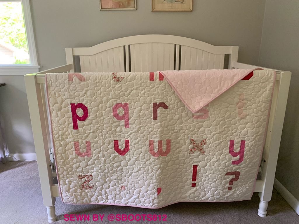 Letter Quilt einer Testnäherin hängt über Babybett